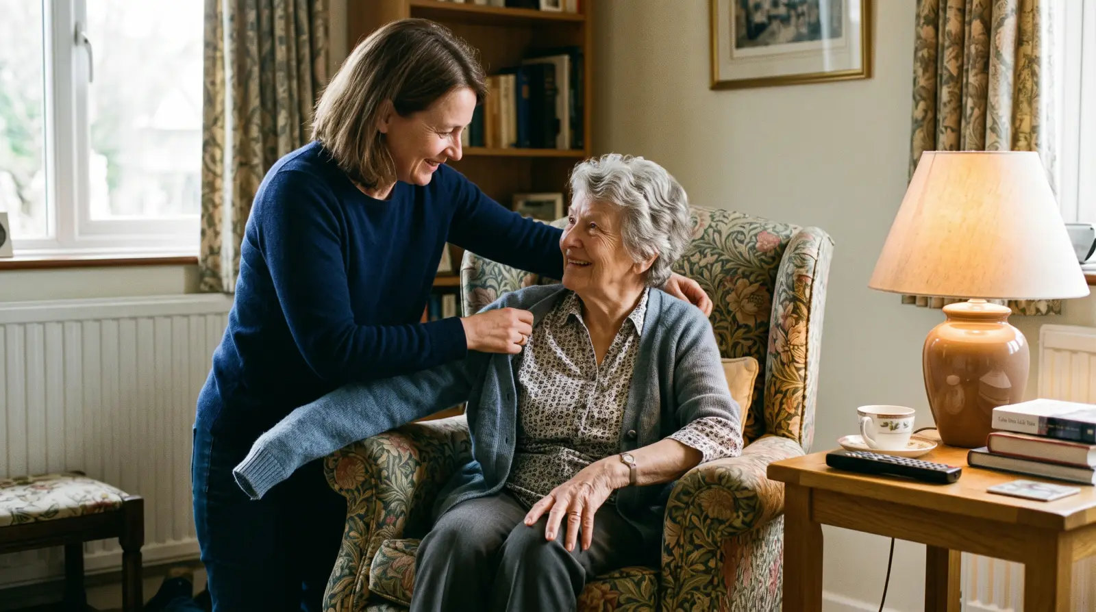 A woman in her early fifties helping her mother in her eighties into a cardigan in a living room